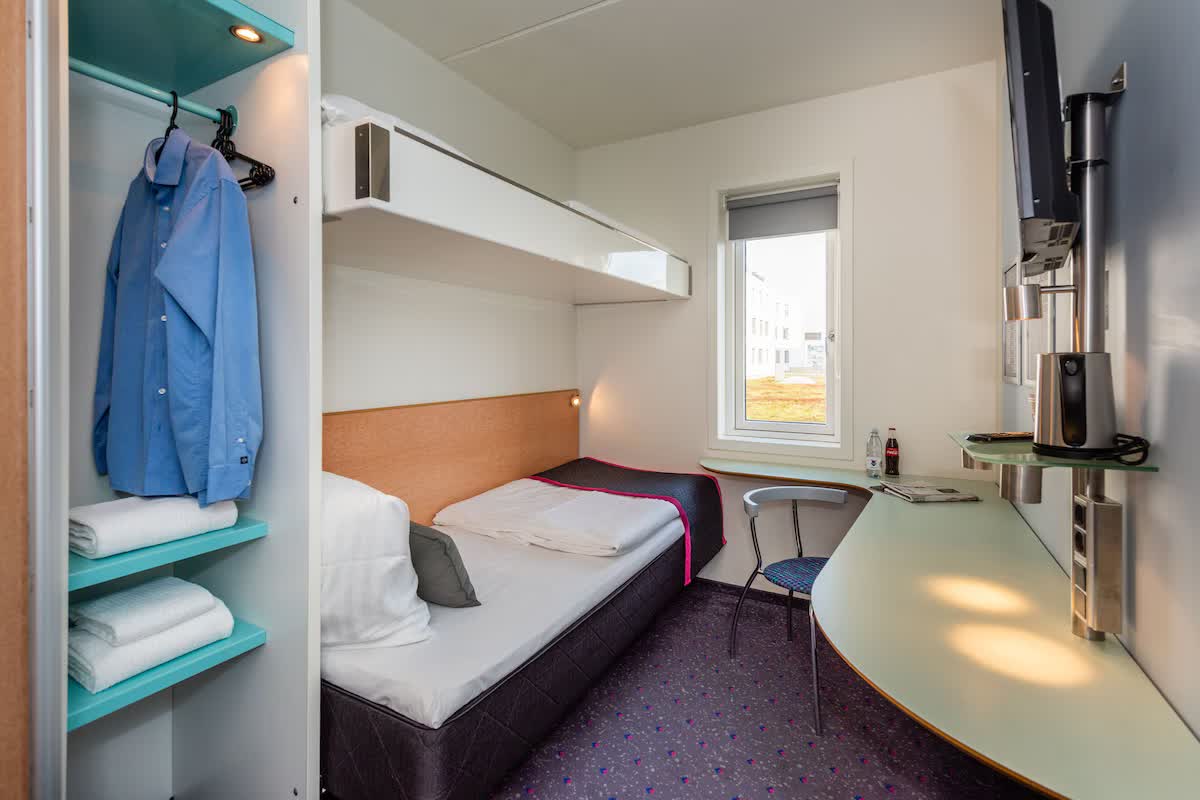 Small uniform hotel room with a berth, a desk surface and a window